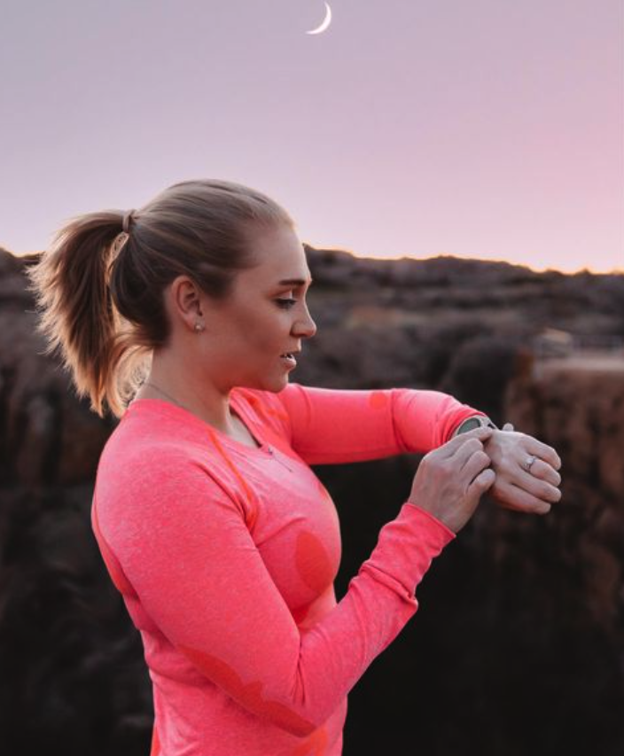 blonde girl in pink shirt running and checking her watch at twilight